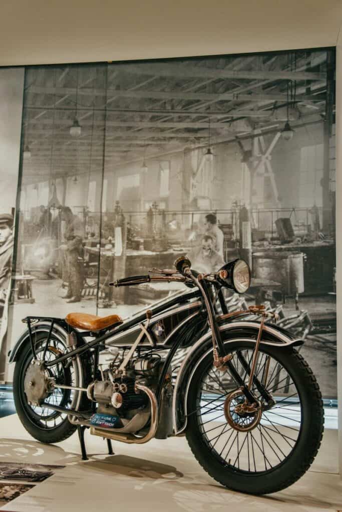 Moto clásica negra con asiento de cuero marrón frente a un mural de una fábrica